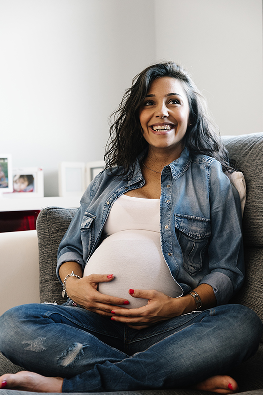 Pretty Pregnant woman sitting on a sofa at home.